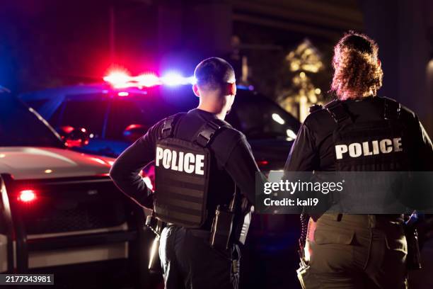 two multiracial police officers working outdoors at night - cuerpo de policía fotografías e imágenes de stock