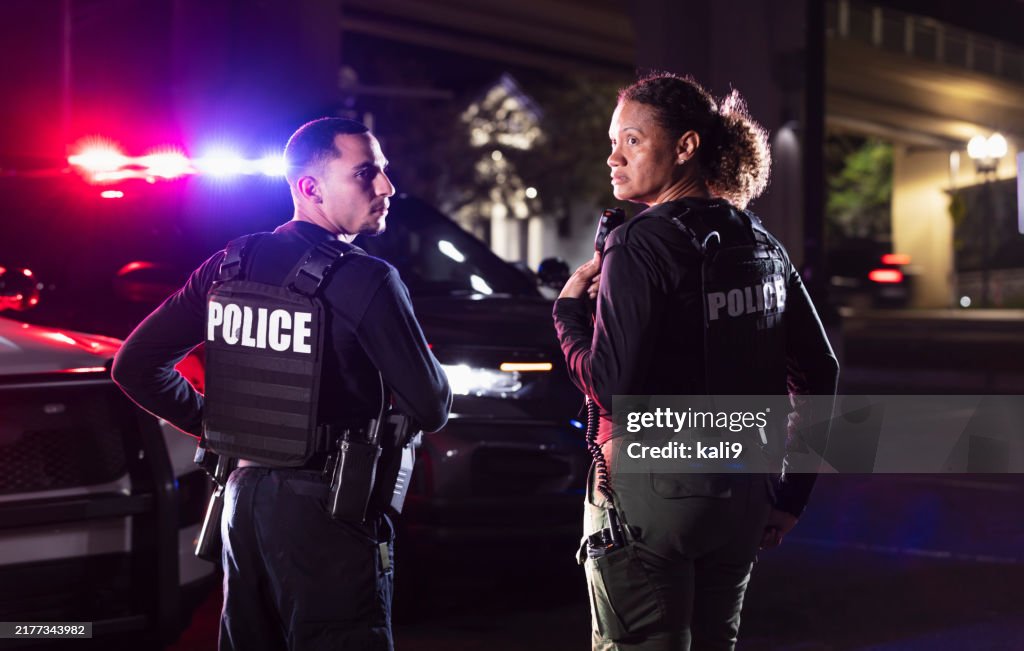 Two multiracial police officers working outdoors at night