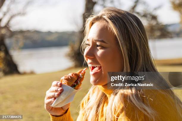 woman savoring a croissant sandwich - autumn lake chair stock pictures, royalty-free photos & images