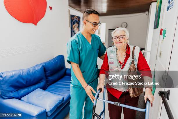 caregiver helping senior woman walk with walker at nursing home - nursing assistant stock pictures, royalty-free photos & images