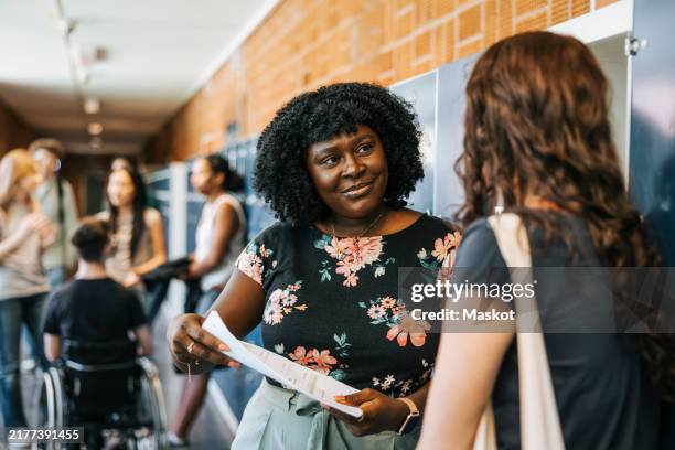 teacher discussing with female student over paper near lockers at high school - schoolbegeleider stockfoto's en -beelden