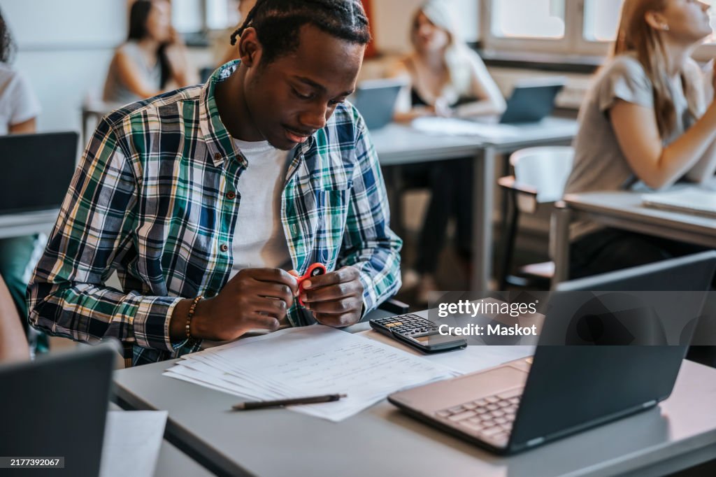 Male high school student with fidget spinner at desk in classroom
