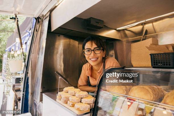 portrait of smiling female food vendor leaning near display in van - furgone ambulante foto e immagini stock