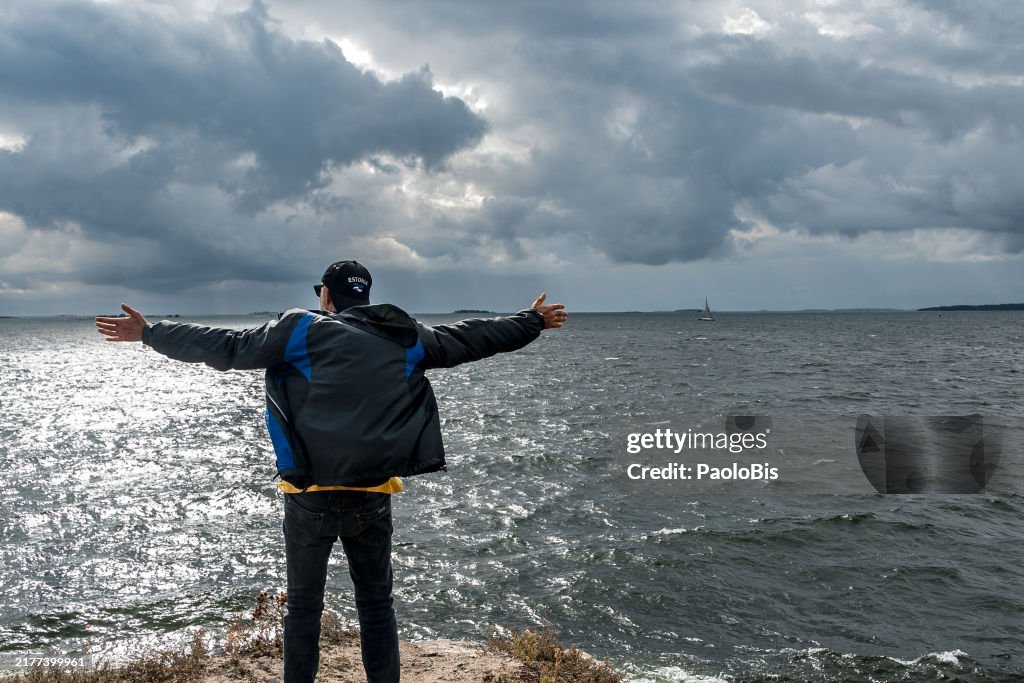 A man with open arms looks out over the Baltic Sea from. Suomenlinna Fortress Islands, Helsinki, Finland