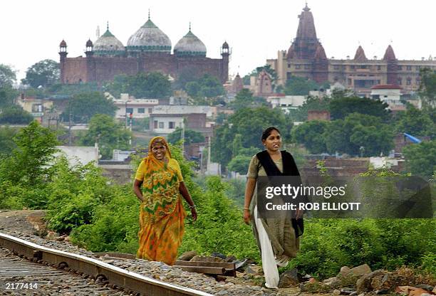 Indian women walk along a railway track where in the distance can be seen the rising domes of the Muslim Shahi Masjid Idgah mosque within the complex...
