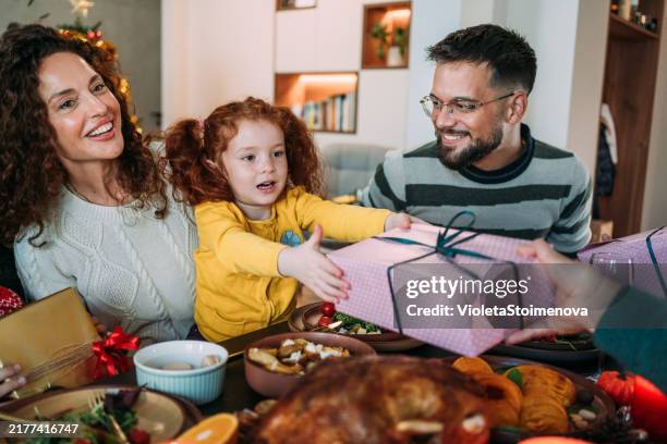 die fröhliche familie versammelt sich um den tisch und tauscht geschenke für weihnachten aus. - gift lounge stock-fotos und bilder