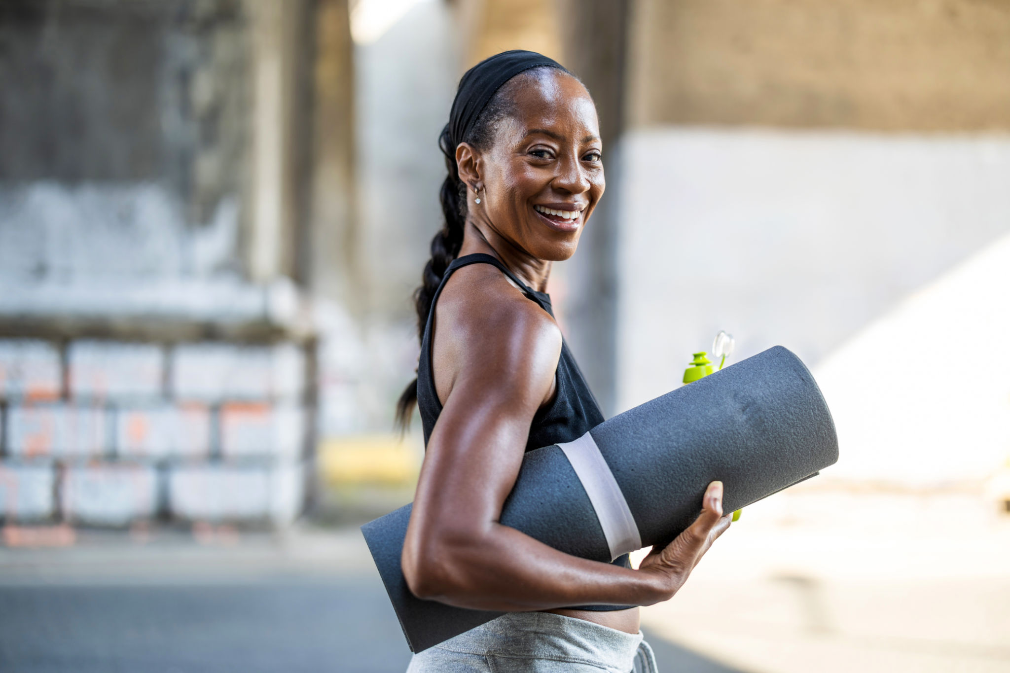 Smiling woman holding an exercise mat in the city street Smiling woman holding an exercise mat in the city street