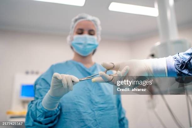 nurse giving surgical forceps to surgeon during surgery - forceps stock pictures, royalty-free photos & images