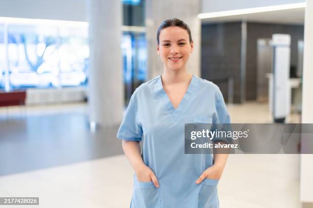 portrait of smiling nurse in hospital hallway with hands in pockets - zuster stockfoto's en -beelden