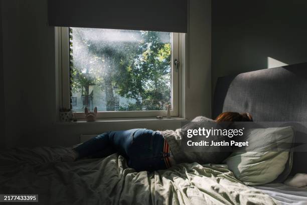 powerful shot of a mature woman lying on her bed with her back to camera - negative emotion - menopause stock pictures, royalty-free photos & images