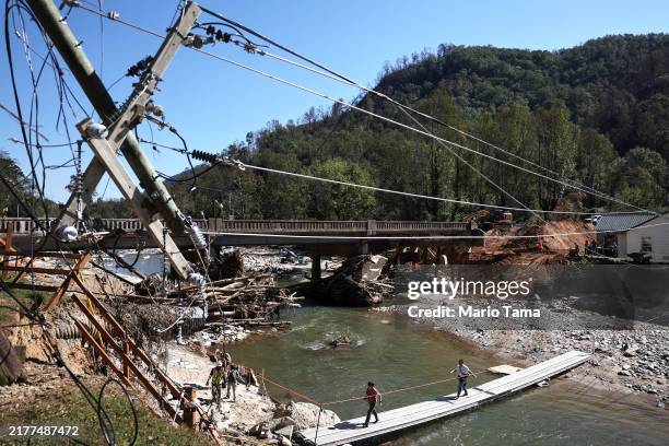 People walk across a makeshift bridge as a damaged bridge is repaired in the aftermath of Hurricane Helene flooding on October 8, 2024 in Bat Cave,...
