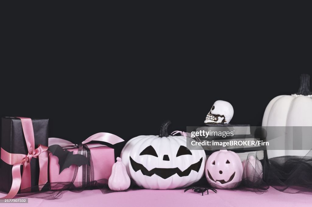 Pink and white Halloween decor with black and white pumpkins, spell books and spiders on black background with copy space