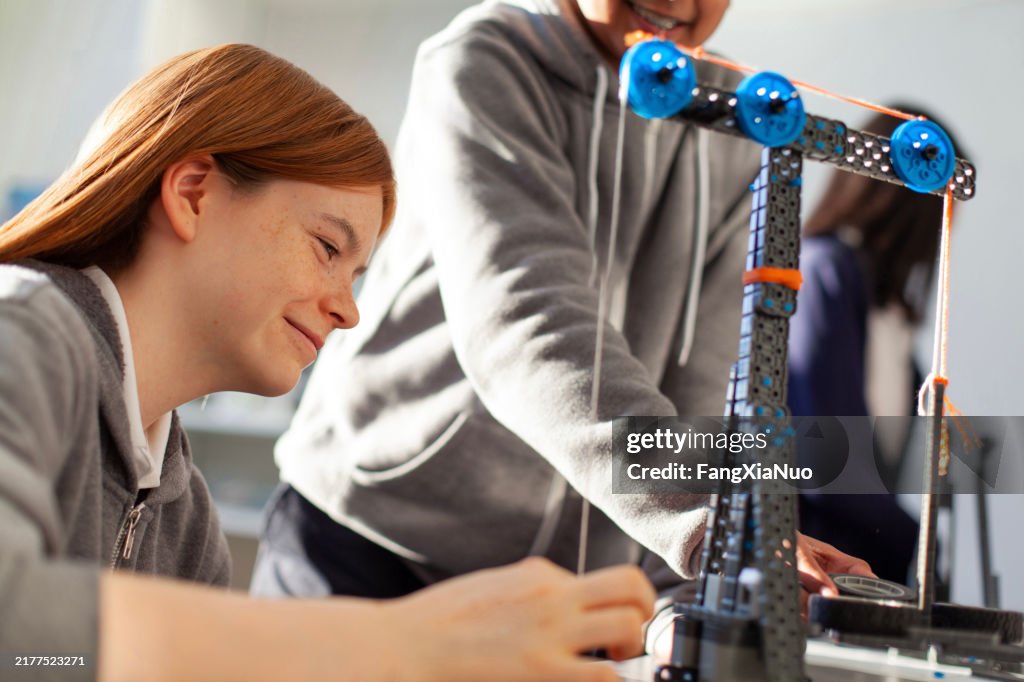Teenage girl in high school classroom making physics construction science engineering technology mathematics STEM project with classmate