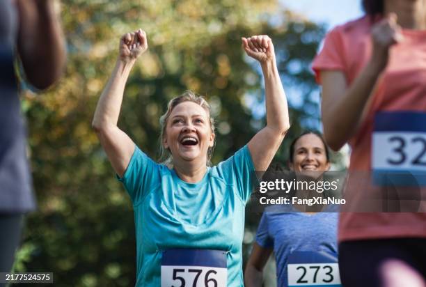 mature woman raising hands in celebration success while running in marathon race with group of women in park - marathon bildbanksfoton och bilder
