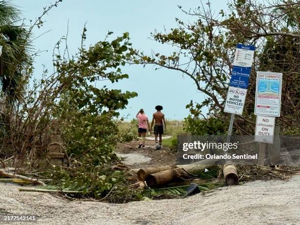 Two beach-goers walk through fallen debris at a public beach access off of Ocean Avenue on Siesta Key, Florida, on Friday, Oct. 11, 2024. The...