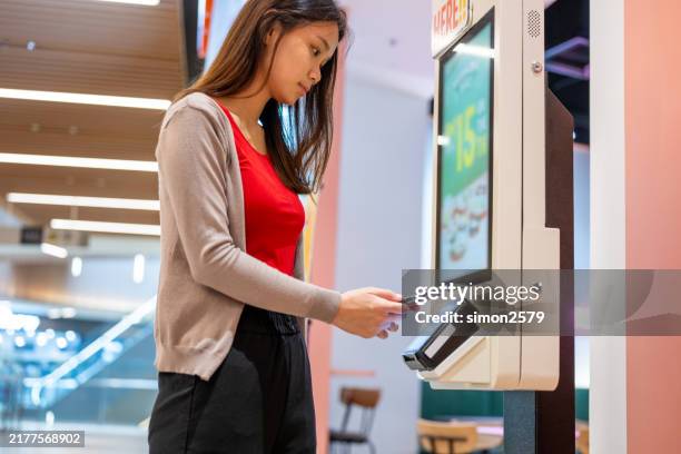 a young asian woman at making a mobile payment at self-service kiosk - restaurant booth stock pictures, royalty-free photos & images