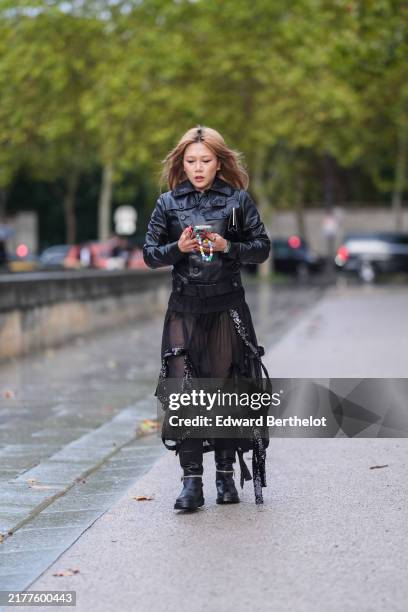 Guest wears a black leather jacket, black transparent gathered long skirt, black leather boots, outside Balenciaga, during Womenswear Spring/Summer...