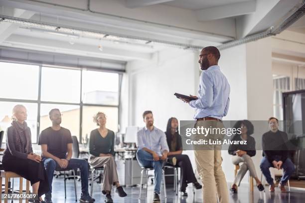 african businessman stands at the front and engaging with colleagues seated for a meeting - treinamento no trabalho imagens e fotografias de stock