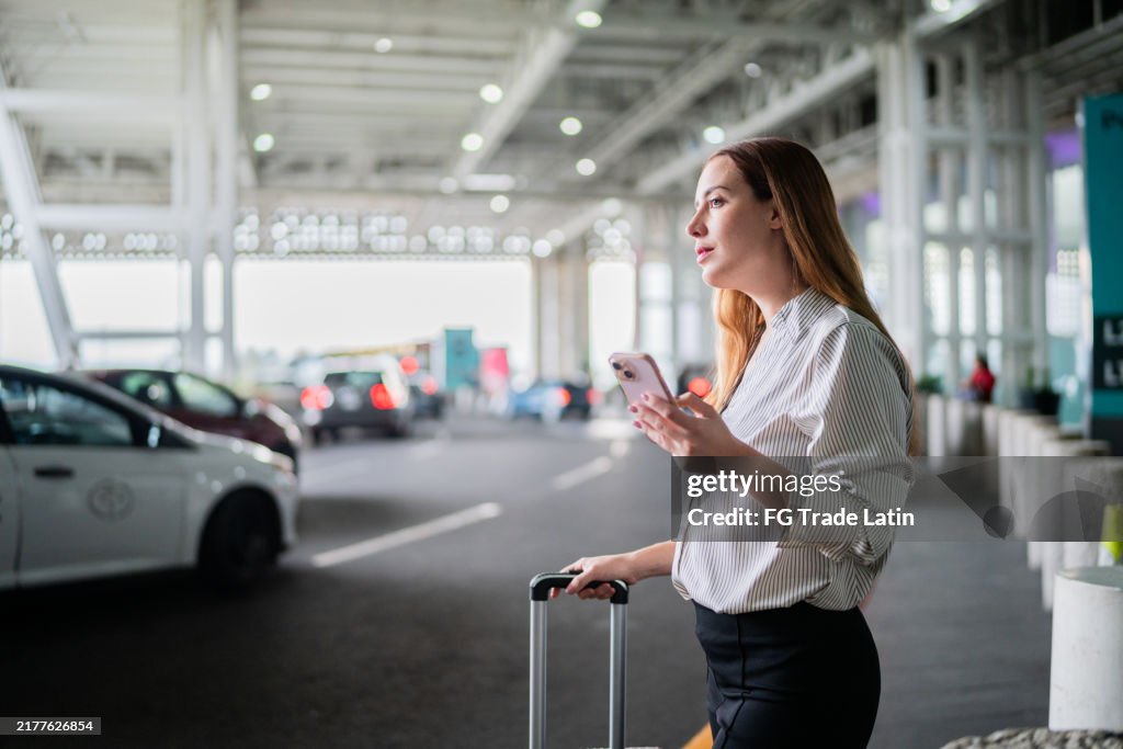 Mid adult businesswoman using mobile phone waiting taxi at airport