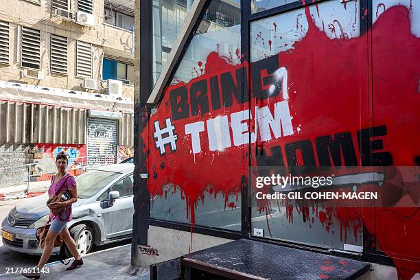 Woman walks past graffiti showing the slogan "#BringThemHome", referring to the remaining hostages held captive in the Gaza Strip by Palestinian...