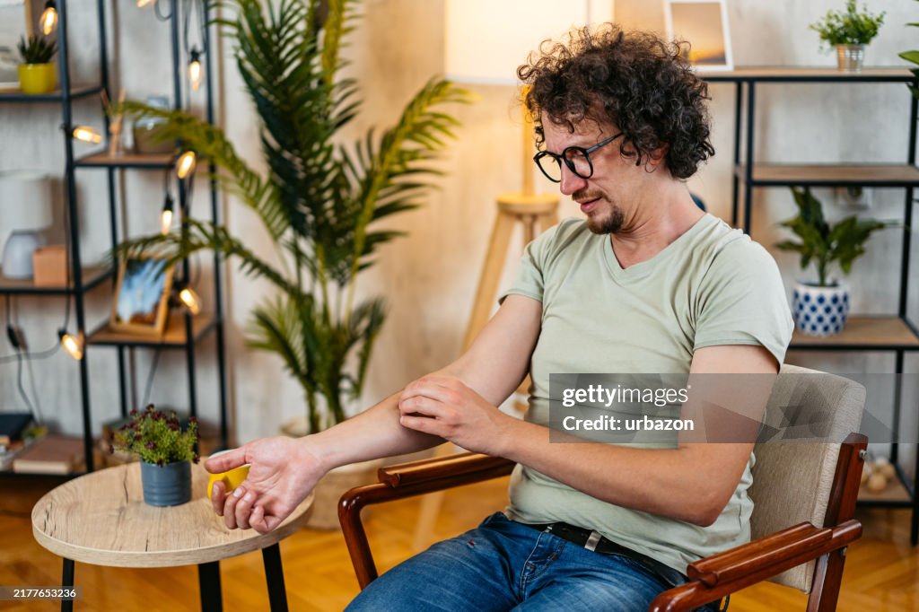 Mid-Adult Man Scratching His Skin While Sitting In An Armchair At Home