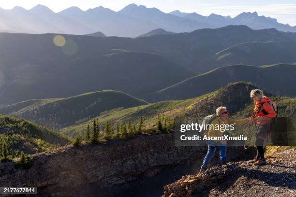 mature mountain climber offers helping hand - mid distance stock pictures, royalty-free photos & images