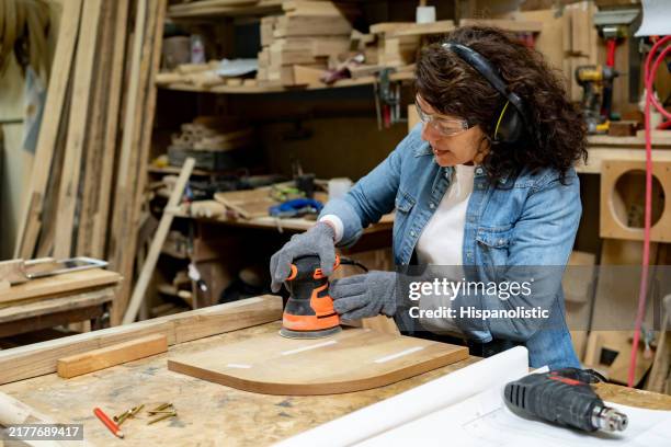 mujer trabajando en un taller de carpintería lijando un trozo de madera - pulidora fotografías e imágenes de stock