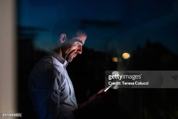 businessman using smartphone by window at night - office block exterior stock pictures, royalty-free photos & images
