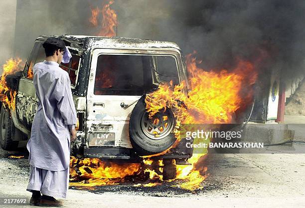 Local resident looks at a burning car set on fire by an angry mob of Shiite Muslims following an attack on a Chiite mosque in Quetta, 04 July 2003....