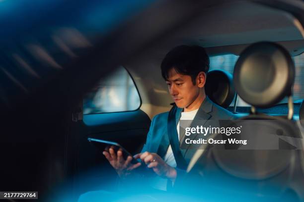 asian male entrepreneur working on digital tablet while traveling by a car - wealth stock pictures, royalty-free photos & images