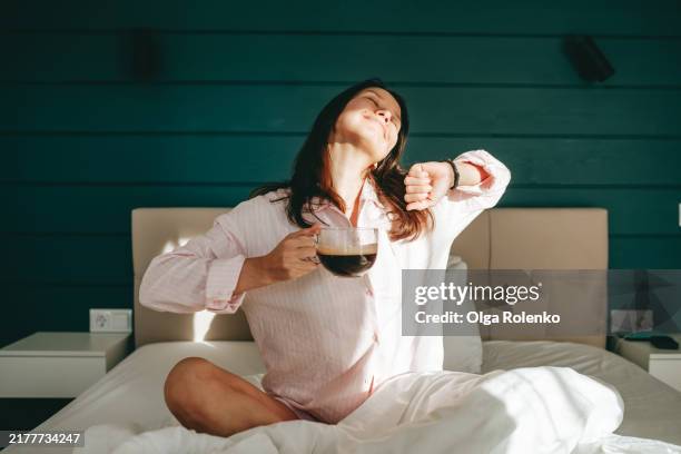 morning stretch: relaxed woman with coffee stretches as sunlight greets her. - ochtend stockfoto's en -beelden