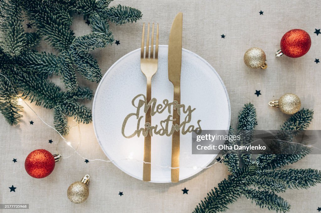 Elegant Christmas table setting with a white plate, golden cutlery, and Merry Christmas text decoration