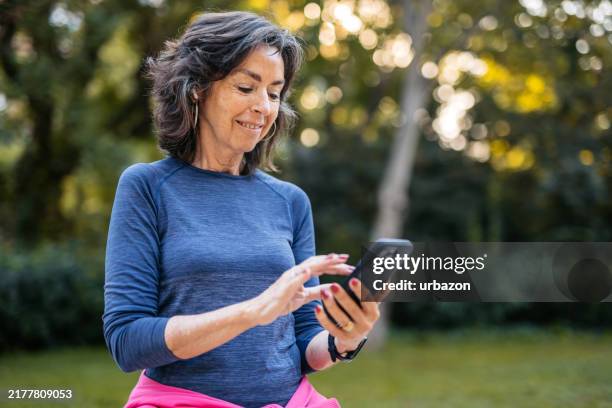 senior woman checking fitness activity on the phone after jogging in a public park in barcelona in spain - bewakingsapparatuur stockfoto's en -beelden