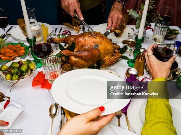 man carving and serving roasted christmas turkey at dinner table - roasted stock pictures, royalty-free photos & images