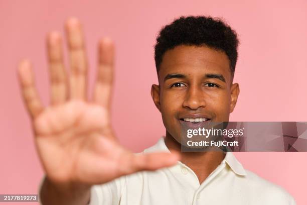 young man making stop gesture with hand on pink background - refusing stock pictures, royalty-free photos & images