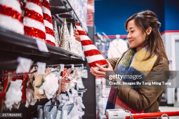 cheerful woman shopping for christmas decoration in a store during festive holiday - ambience store stock pictures, royalty-free photos & images