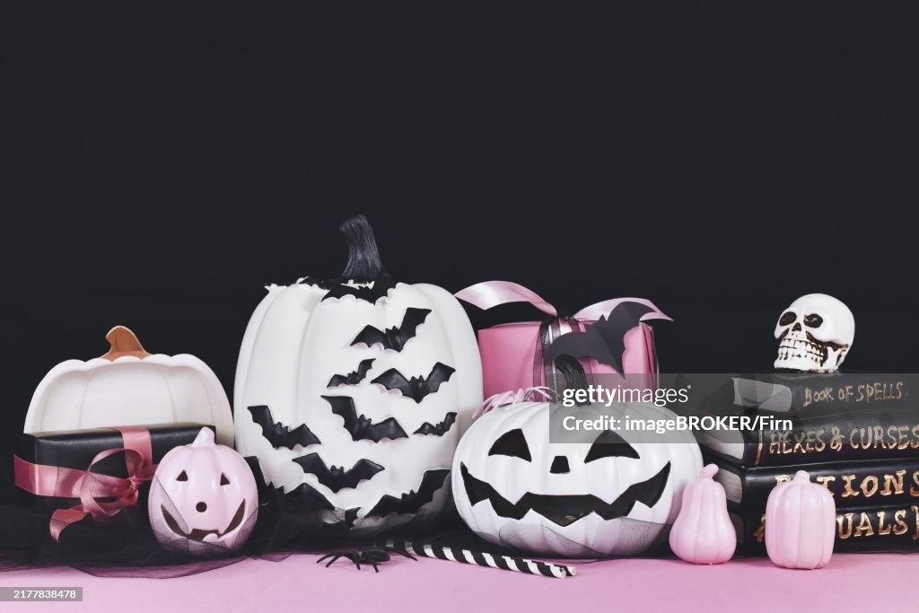 Pink and white Halloween decor with black and white pumpkins, spell books and spiders on black background with copy space