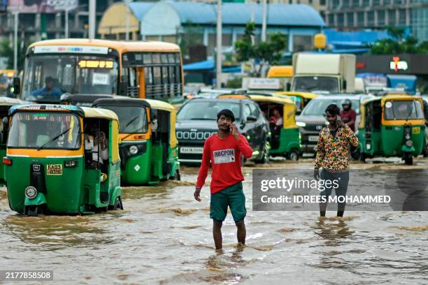Commuters wade through a flooded road following heavy rainfall in Bengaluru on October 15, 2024.