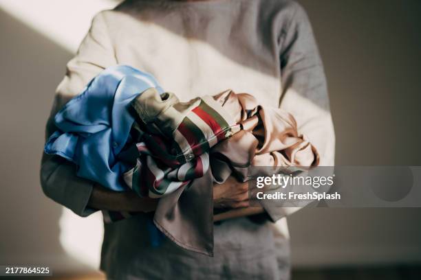 person holding a stack of colorful clothes in warm light - vestido de cetim imagens e fotografias de stock