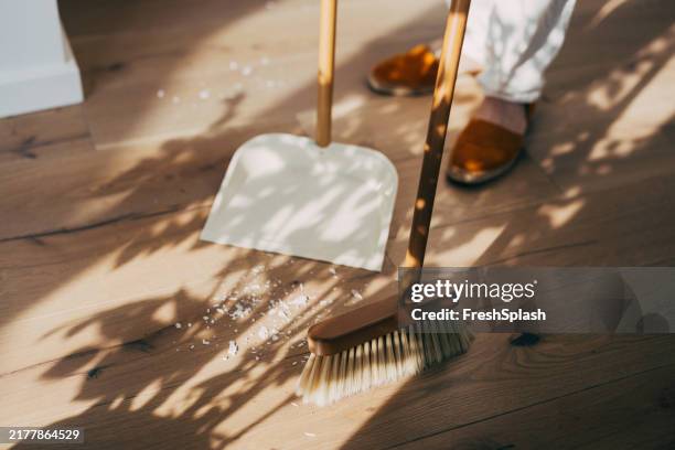 sweeping wooden floor with brush and dustpan in sunlit room - vegen stockfoto's en -beelden