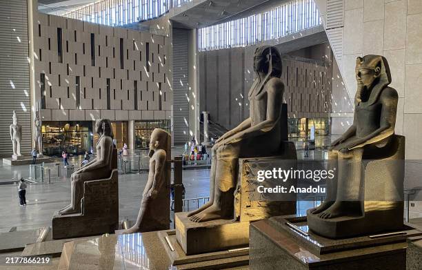 View of sunlight pouring into the Grand Egyptian Museum's main hall, illuminating a row of colossal statues of pharaohs seated in regal poses at the...