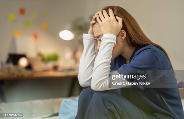 stress asian woman in blue scrubs sitting bed in a thoughtful head in her hands, suffering from emotional exhaustion mental pressure - physical pressure stock pictures, royalty-free photos & images