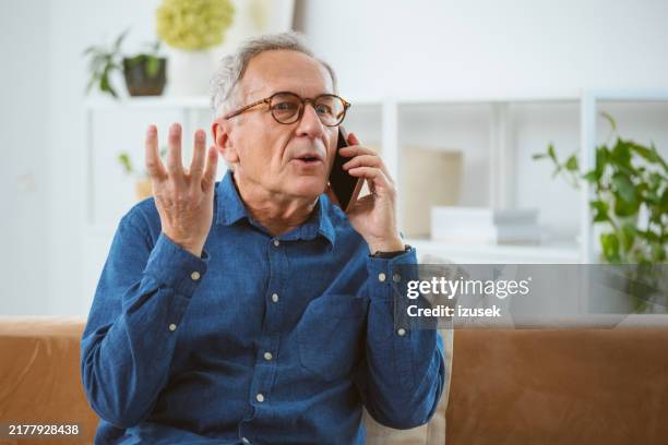 un homme âgé mécontent qui parle au téléphone - irritation photos et images de collection