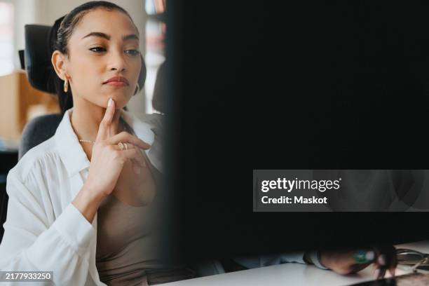 young business professional with hand on chin looking at computer screen while working in office - cursor computer stock pictures, royalty-free photos & images