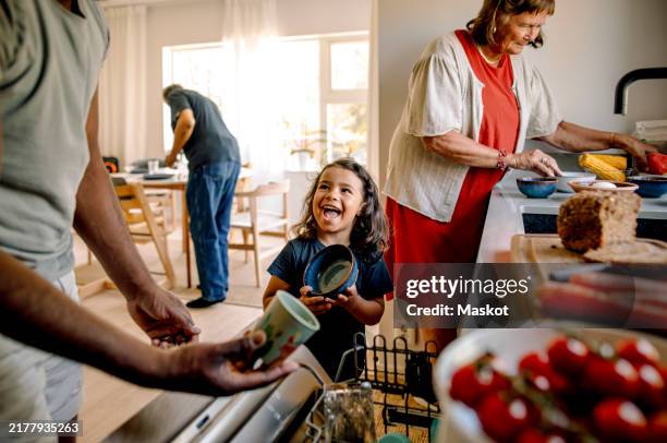 happy son holding bowl while standing in kitchen with family at home - caricare attività foto e immagini stock