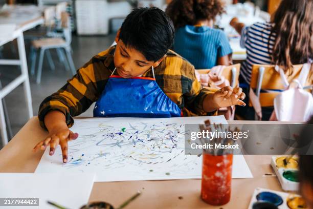 focused boy doing finger painting on paper during art class at elementary school - finger painting stock pictures, royalty-free photos & images