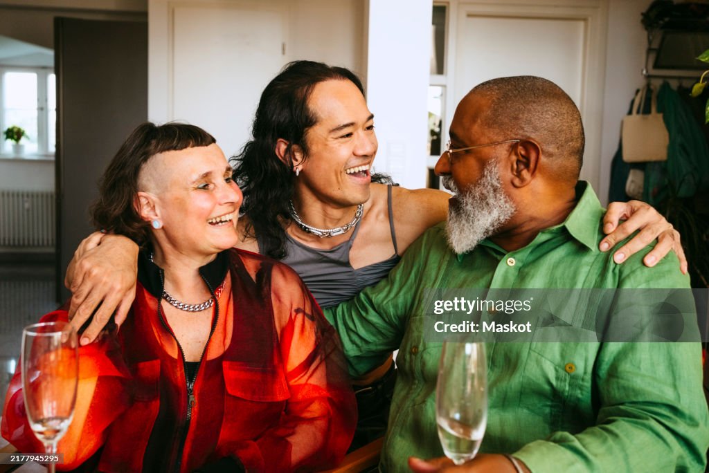 Happy gay man with arms around LGBTQ friends at dinner party