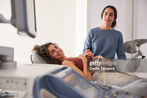 la joven madre y su esposa observan la pantalla de ultrasonido con expresiones de esperanza. - análisis ginecológico fotografías e imágenes de stock