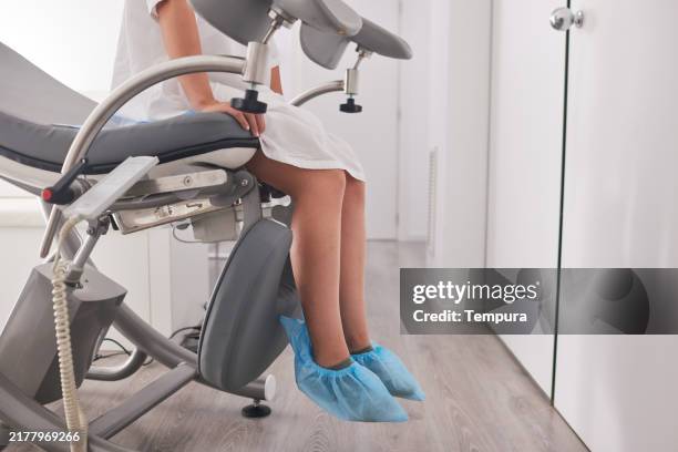 die junge frau im krankenhauskittel sitzt auf einem gynäkologenstuhl und wartet ruhig. - gynäkologe stock-fotos und bilder