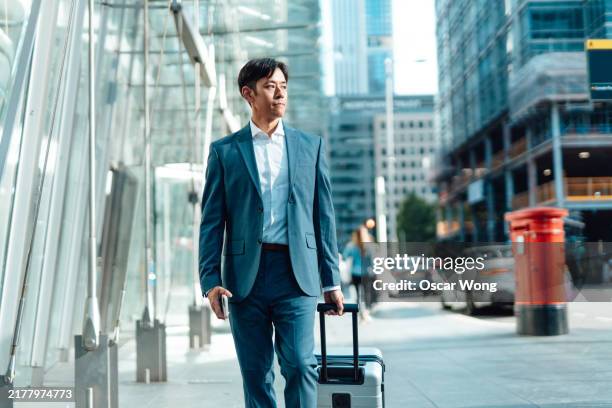 asian businessmen walking on city street with luggage - airport departure board stock pictures, royalty-free photos & images